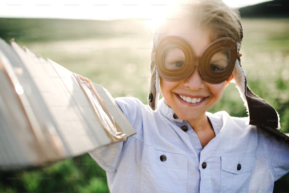 A close-up of a small boy playing on a meadow in nature, wearing pilot goggles and wings.