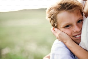 A close-up of small boy hugging his unrecognizable mother outdoors in nature. A copy space.