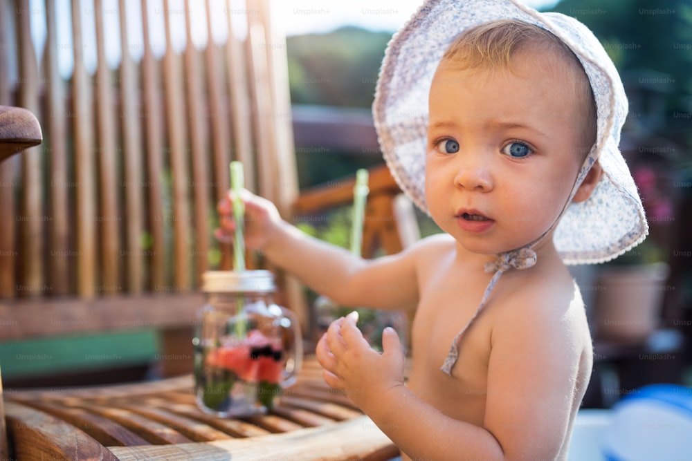 A small girl with a fruit drink standing by a table on a patio in summer.