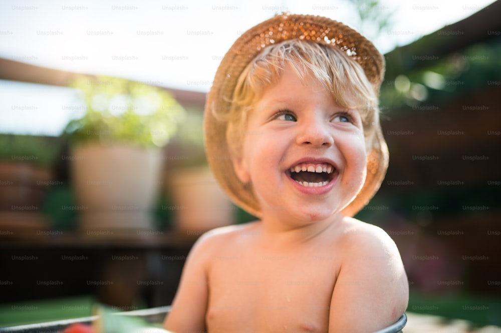Ein kleiner Junge mit Hut im Sommer oben ohne im Garten und lacht. Speicherplatz kopieren.