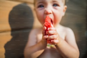 Um close-up de menina pequena ao ar livre no verão, comendo melancia.
