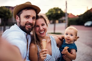 Pais e menina pequena com sorvete ao ar livre no verão, rindo ao tirar selfie.