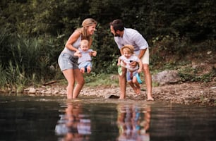 A young family with two toddler children spending time outdoors by the river in summer, having fun.