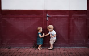 Deux petits enfants en bas âge à l’extérieur en été, mangeant de la crème glacée et se tenant devant une porte.