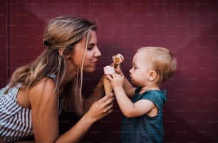 A young mother with small toddler girl outdoors in summer, eating ice cream.