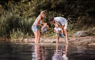 A young family with two toddler children spending time outdoors by the river in summer, having fun.