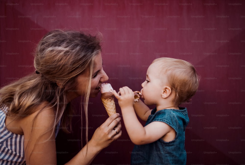 Eine junge Mutter mit kleinem Kleinkind im Sommer draußen und isst Eis.