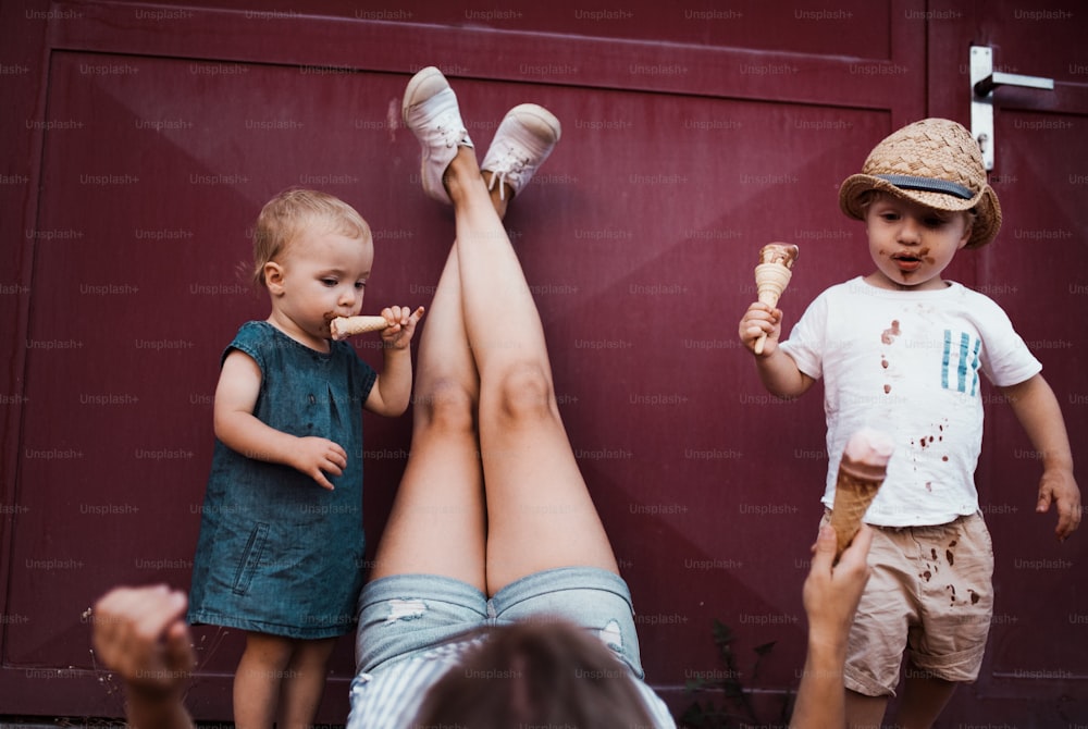 Uma jovem mãe irreconhecível com duas crianças pequenas ao ar livre no verão, comendo sorvete.