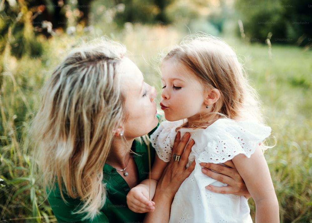 Young mother with small daughter on a meadow in nature, kissing.