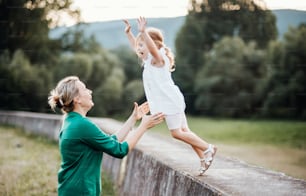 Young mother in nature with small daughter, having fun. A girl jumping into mother's arms.