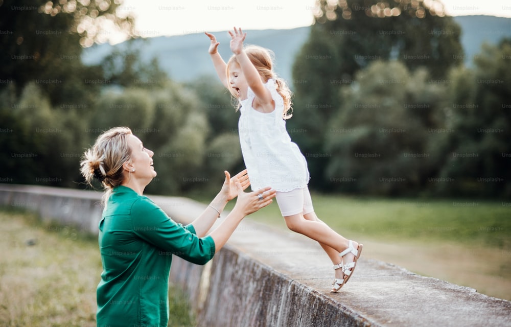 Jovem mãe na natureza com filha pequena, se divertindo. Uma menina pulando nos braços da mãe.