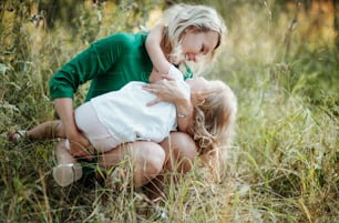 Beautiful young mother in green sunny summer nature holding her cute small daughter.