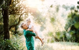 Beautiful young mother in green sunny summer nature holding her cute small daughter in the arms. Copy space.