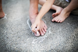 여름날 공원의 도로에서 아버지의 발의 윤곽을 그리는 작은 소년의 중간 부분.