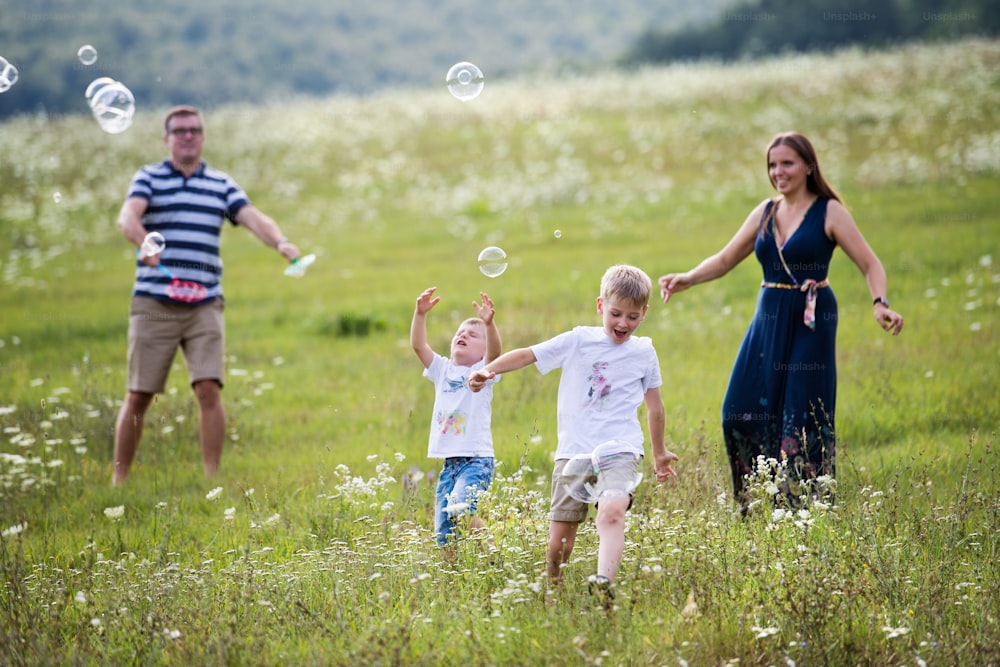 A young family with two small cheerful sons walking in nature on a summer day, blowing soap bubbles.