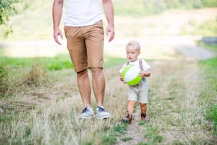 Unrecognizable young father with a small toddler son walking in sunny summer nature. A midsection.