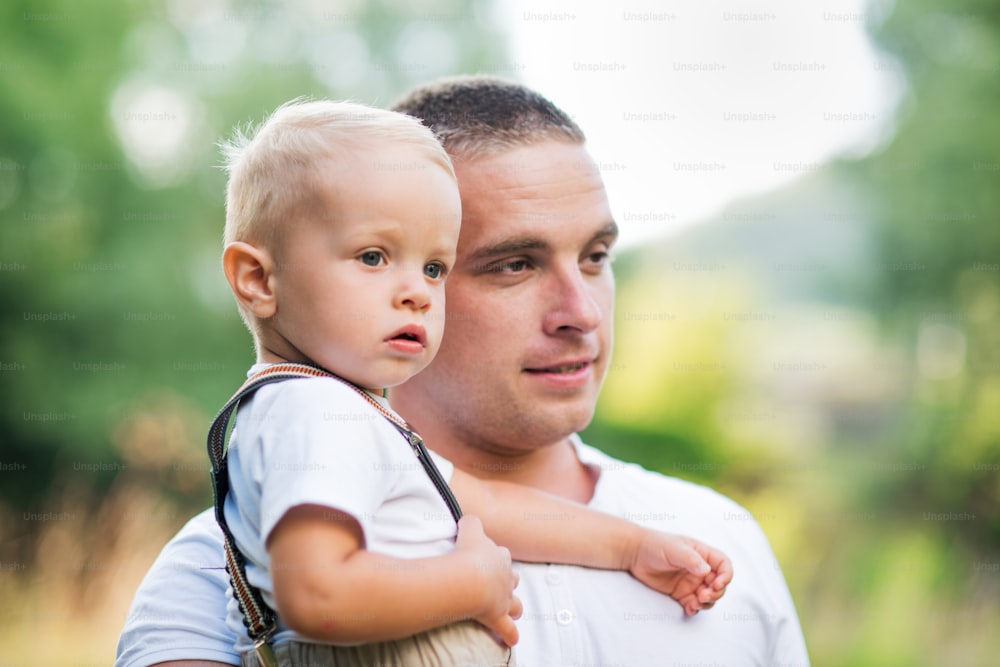 Young father holding a small toddler son in sunny summer nature. A close-up.