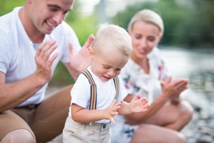 Un bambino piccolo e felice con i suoi genitori fuori nella soleggiata natura estiva, applaudendo.