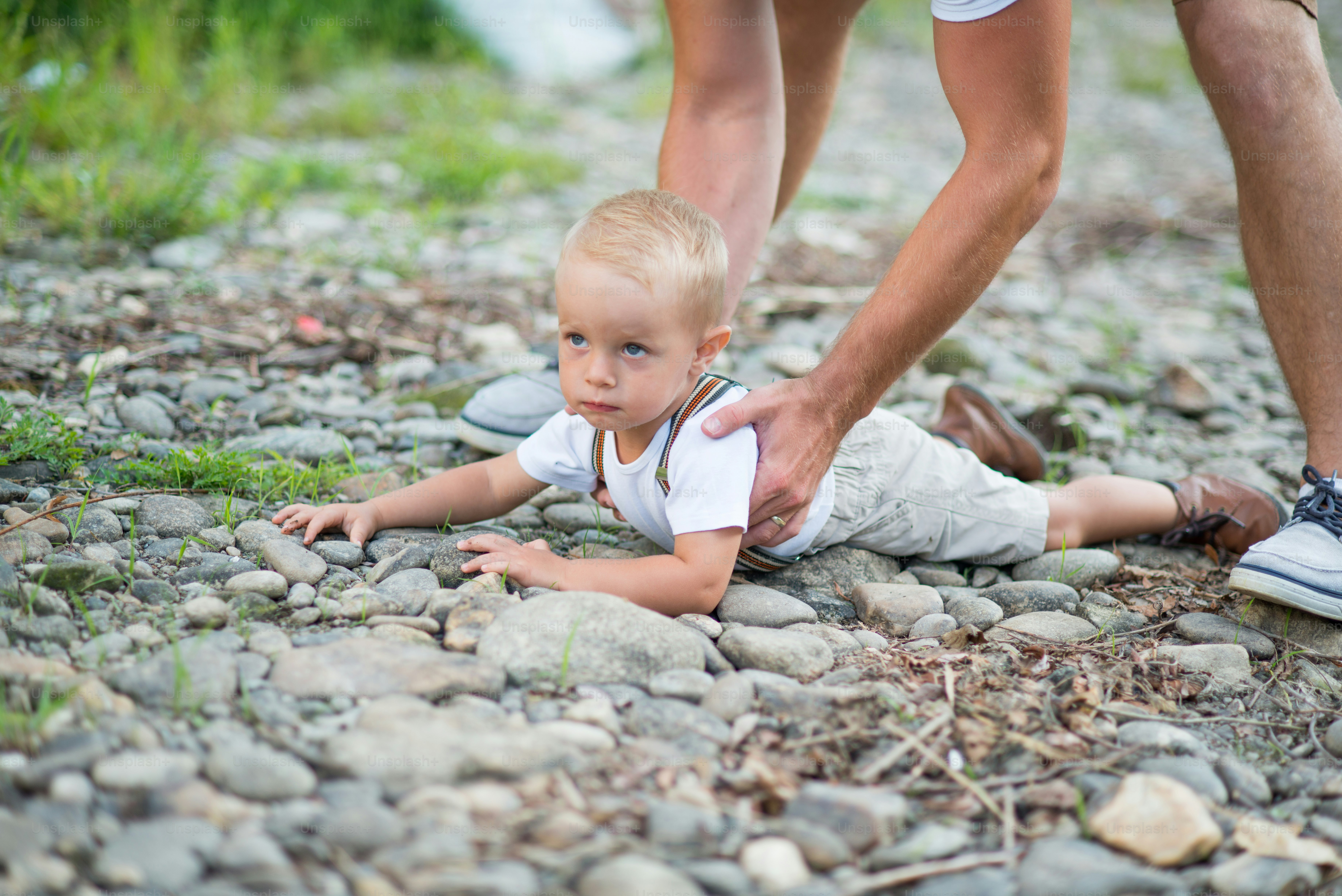 Padre irreconocible levantando a un pequeño hijo pequeño del suelo en la soleada naturaleza del verano.