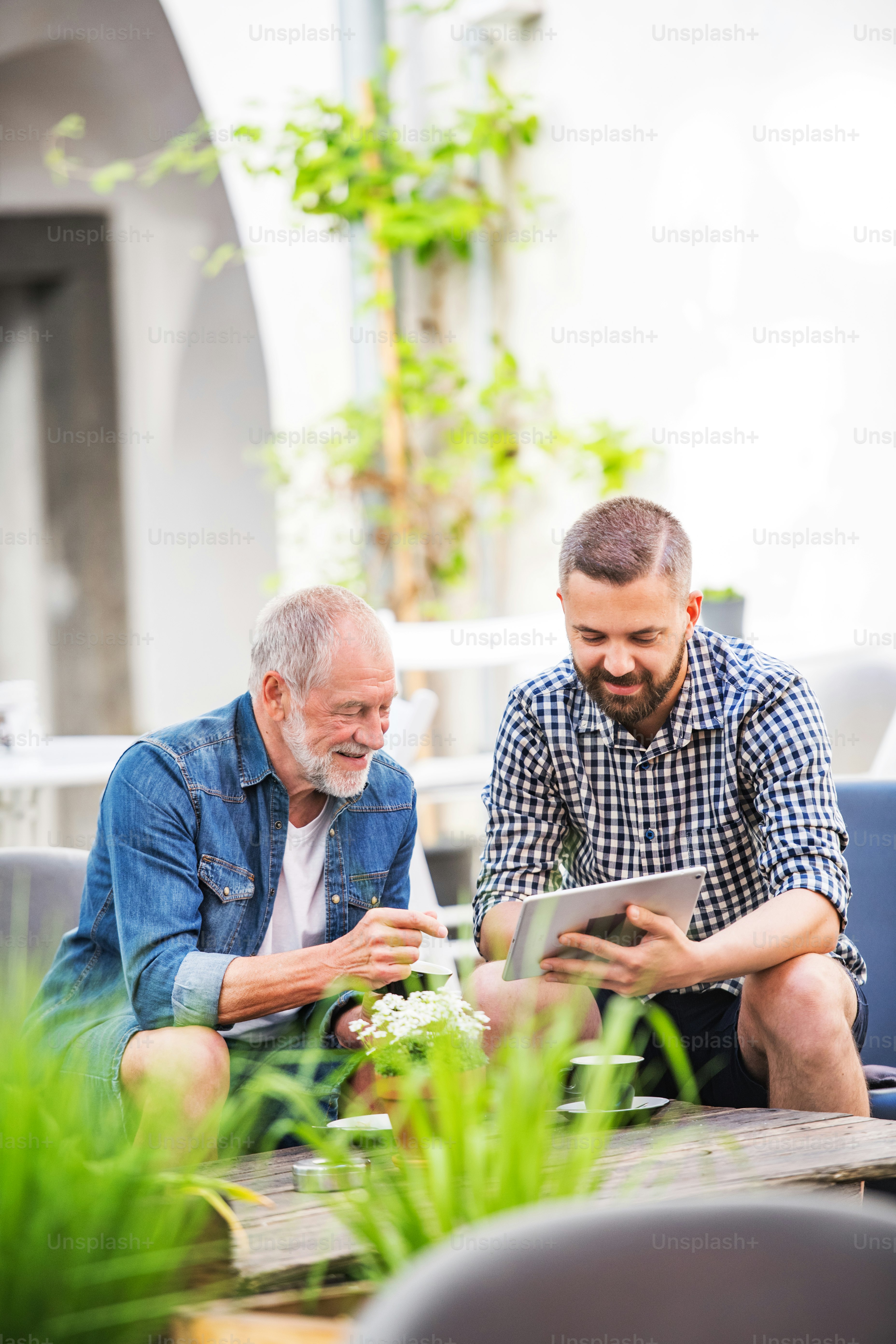 Ein glücklicher erwachsener Hipster-Sohn mit Tablet und älterem Vater in einem Café in der Stadt.