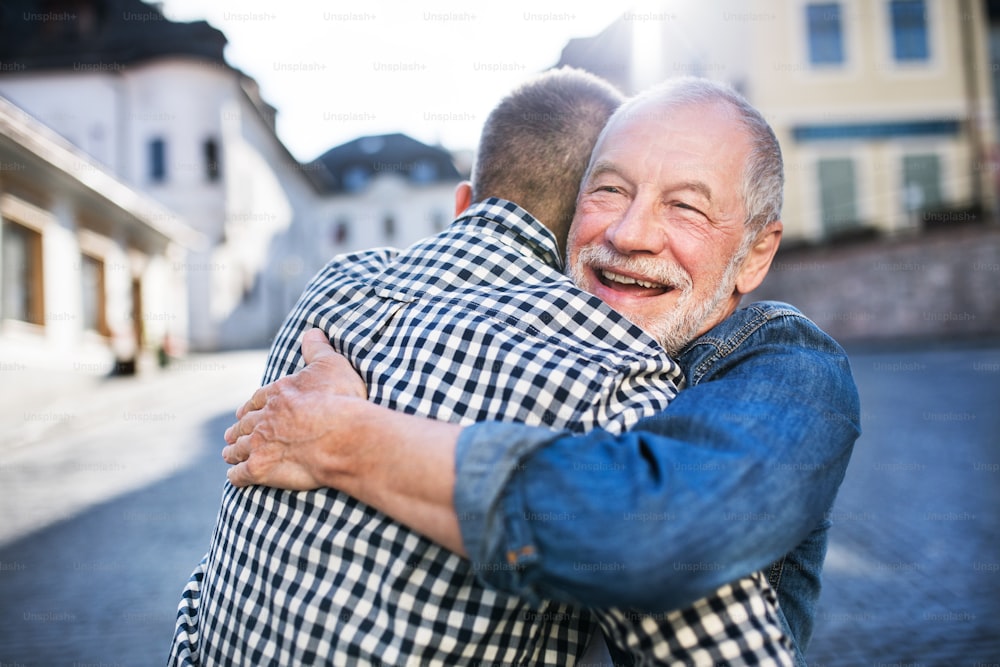 Un figlio hipster adulto e il suo felice padre anziano in città, abbracciati.