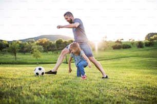 Happy father with a small daughter playing with a ball in spring nature at sunset.