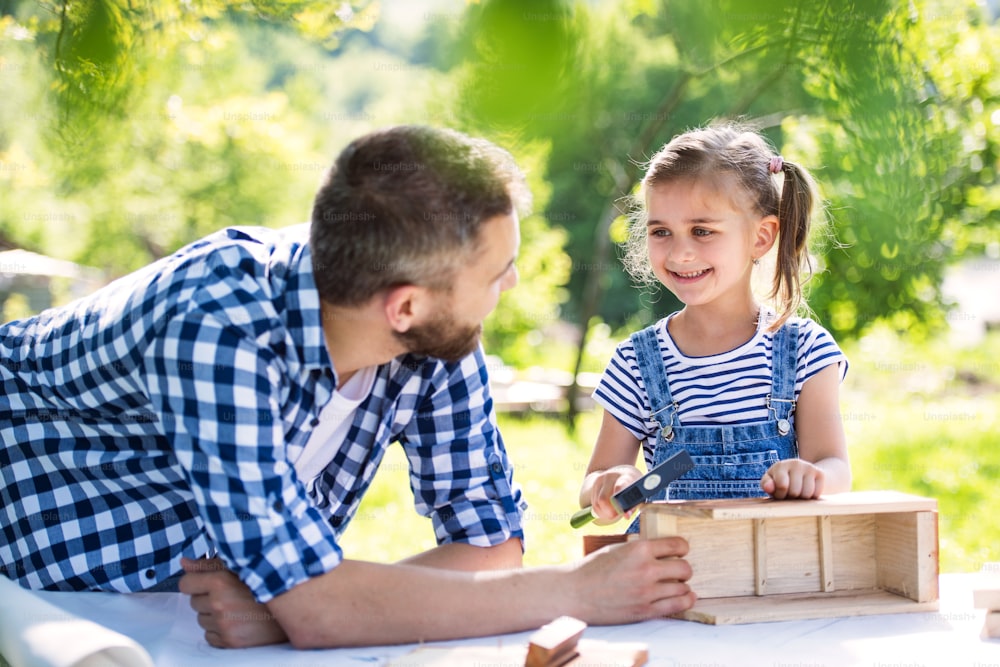 Father with a small daughter outside, making wooden birdhouse or bird feeder.