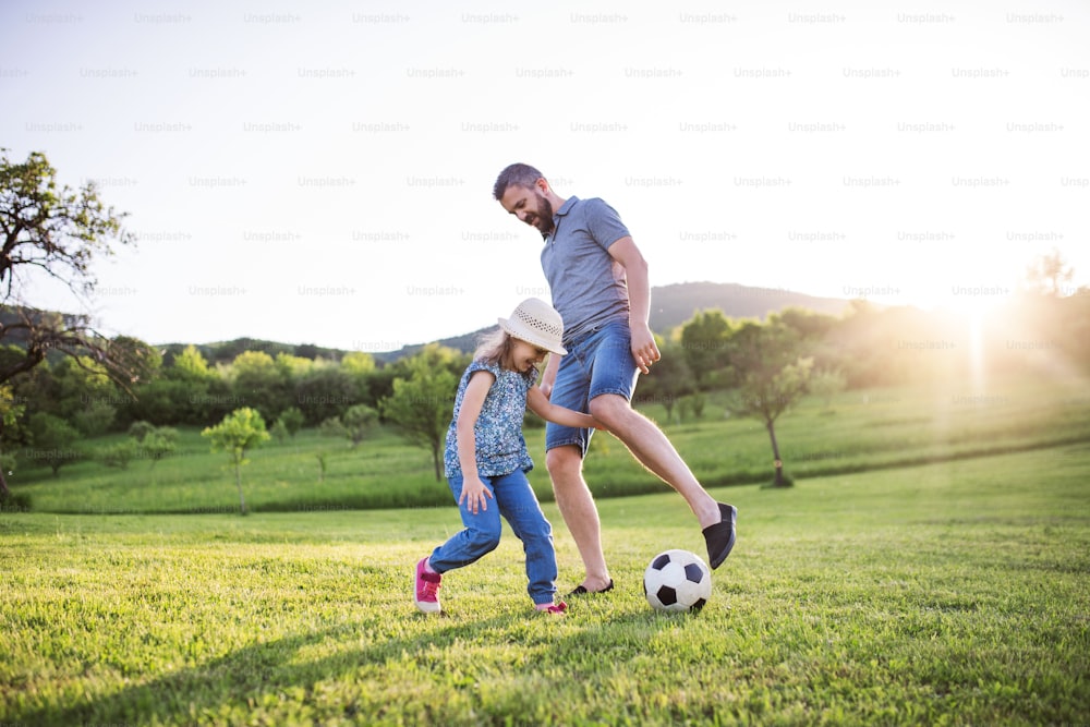 Padre con una hija pequeña jugando con una pelota en la soleada naturaleza primaveral.