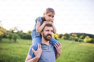 Mature father giving a small daughter a piggyback ride in spring nature.