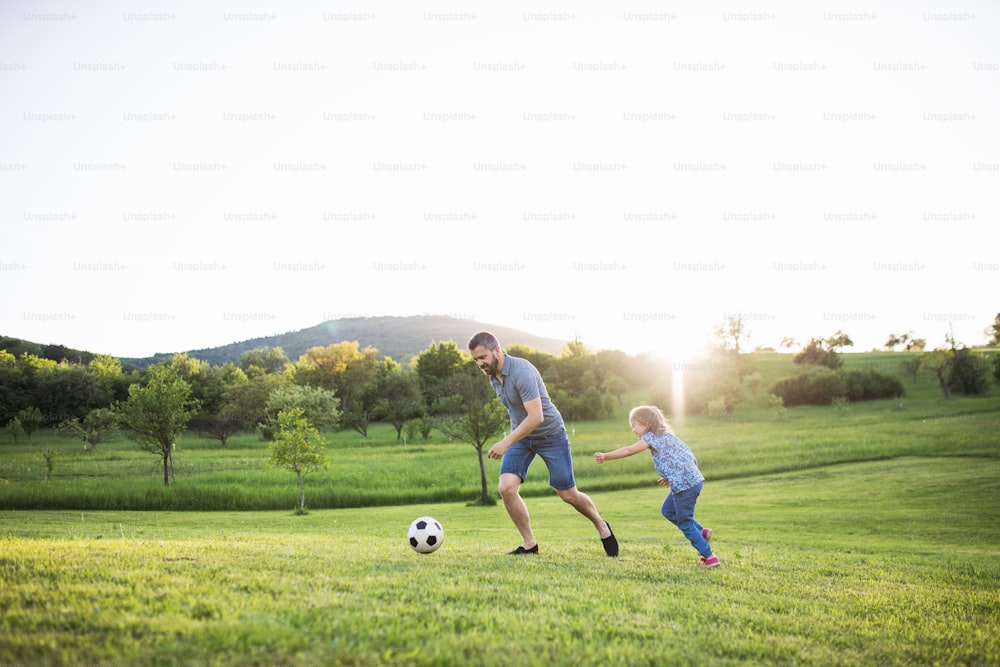 Père avec une petite fille jouant avec un ballon dans la nature printanière ensoleillée.