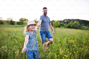 Un padre guapo con una hija pequeña corriendo en la naturaleza primaveral.