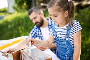 Mature father with a small daughter outside, painting. Wooden birdhouse or bird feeder making.