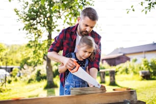 Father and a small daughter with a saw outside, making wooden birdhouse or bird feeder.