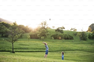 Pai com uma filha pequena brincando com uma bola na natureza da primavera ao pôr do sol.