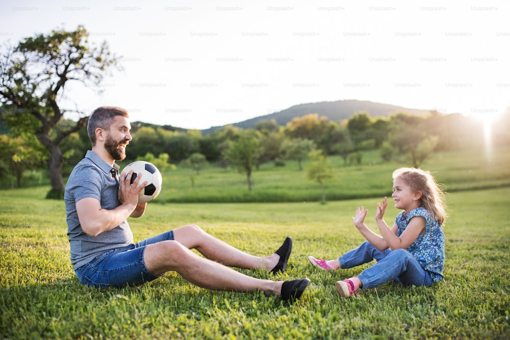 Vater mit einer kleinen Tochter, die mit einem Ball in sonniger Frühlingsnatur spielt.