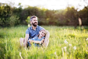 Padre maduro con una hija pequeña sentada en la hierba en la soleada naturaleza primaveral. Espacio de copia.