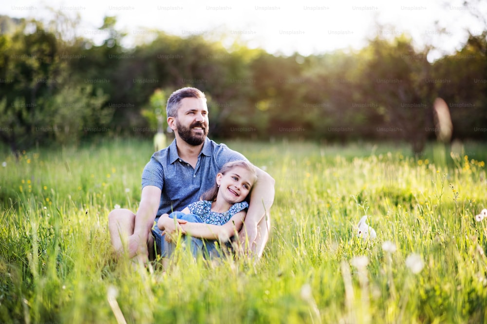 Pai maduro com uma filha pequena sentada na grama na natureza ensolarada da primavera. Espaço de cópia.
