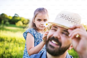 Père avec une petite fille s’amusant avec un chapeau dans la nature printanière ensoleillée.
