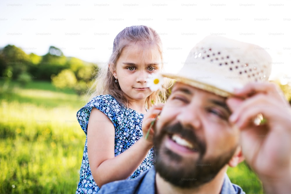 晴れた春の自然の中で帽子をかぶって楽しむ小さな娘を持つ父親。