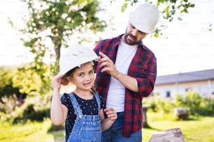 Vater mit einer kleinen Tochter, die sich mit weißen Helmen im Garten amüsiert. Frühling Natur.