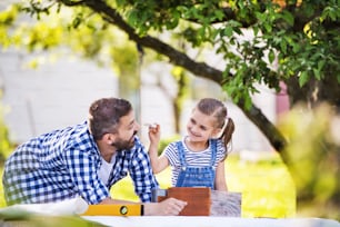 Père avec une petite fille à l’extérieur, fabriquant un nichoir en bois ou une mangeoire à oiseaux.