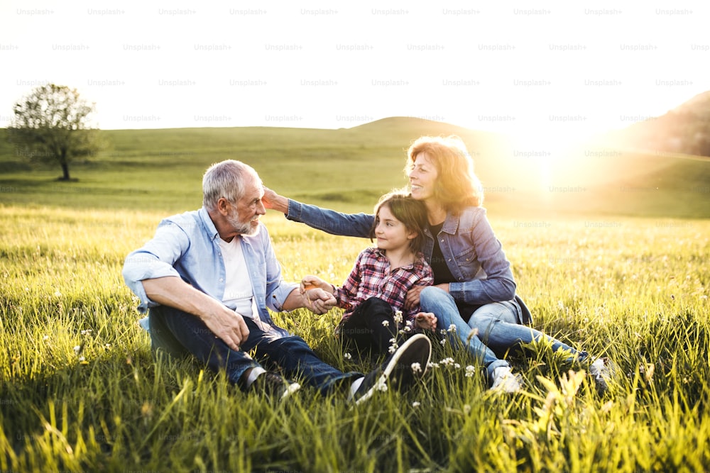 A senior couple with granddaughter outside in spring nature at sunset.