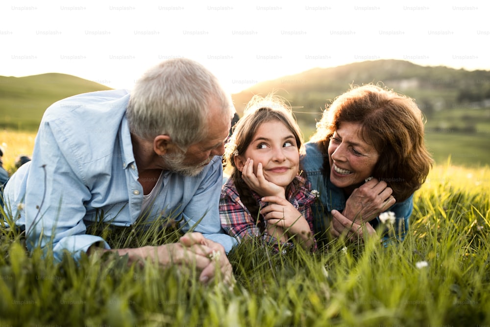 Close-up of a senior couple with granddaughter outside in spring nature, lying on the grass and relaxing.