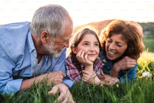 Senior couple with granddaughter outside in spring nature, lying on the grass and relaxing. Close up.
