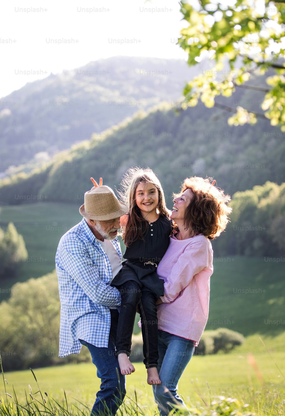Cheerful senior couple with granddaughter outside in spring nature, relaxing and having fun.
