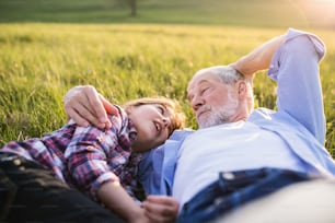 Una bambina con il nonno fuori nella natura primaverile, sdraiata sull'erba, rilassante.