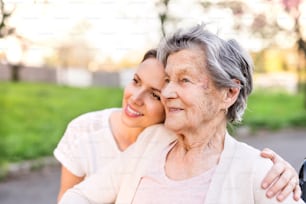 Elderly grandmother and an adult granddaughter outside in spring nature, hugging.