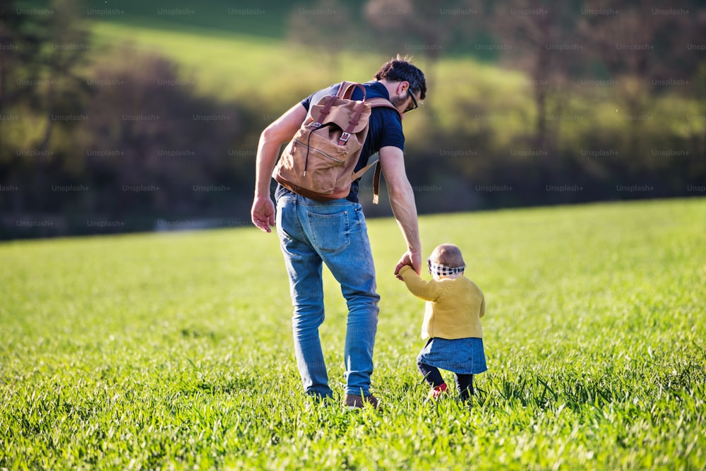 Un padre con su hija pequeña en un paseo al aire libre en la naturaleza verde y soleada de primavera. Vista trasera.
