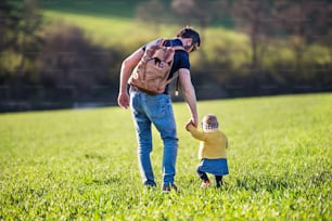 Un padre con su hija pequeña en un paseo al aire libre en la naturaleza verde y soleada de primavera. Vista trasera.