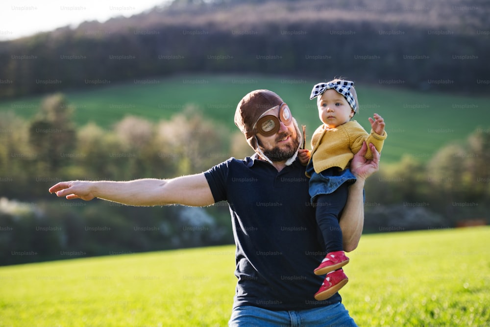 A crazy father with his toddler daughter outside in green sunny spring nature.